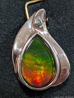 Front view of silver pendant showcasing iridescent teardrop ammolite gemstone with colors of green, orange, and red and small blue accent stone.