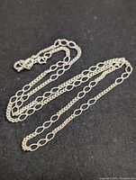 Photo showing full length of the silver chain on a black background to highlight its appearance and alternating link design.