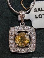 Close-up front view of square silver pendant with citrine center stone and cubic zirconia halo on silver snake chain.