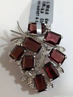 Close-up image showing the silver brooch with seven deep red rectangular garnet stones and multiple clear cubic zirconia stones in prong settings.