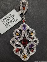 Front view of the sterling silver multi-gemstone pendant displaying the arrangement of garnet, amethyst, citrine, and clear stones and the weight and carat tag.