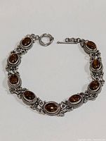 View of the full silver gemstone bracelet laid flat showing amber-colored oval stones in detailed silver settings with toggle clasp.