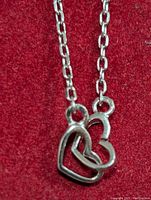 Close-up of the double heart pendant of the silver necklace on a red fabric background, showing detail of the interlinked hearts and chain.