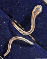 Top close-up view of the silver snake ring on a dark blue fabric background, highlighting the snake's head with eye details and the tail end.