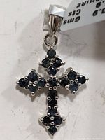 Close-up image of silver cross pendant set with multiple faceted blue sapphires with total weight 1.9ct and pendant weight 3.9g, front view