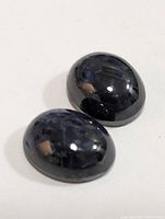 Two polished oval cabochon treated star sapphires with characteristic star effect on white background.