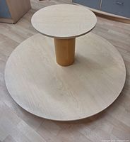 Side view of two-tier round laminated display unit showing smaller upper tier on central cylindrical support above large lower tier.