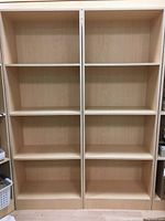 Front view of two side-by-side custom laminated bookcases showing natural wood grain finish and multiple fixed shelves on each unit.
