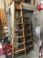 Two wooden step ladders leaning against a door: one taller 8 ft ladder and one smaller folding 6 ft double-sided ladder with visible wear and paint marks.