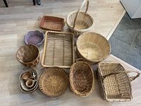 Twelve assorted baskets arranged on a light wood floor showing a variety of shapes and sizes including round, oval, rectangular, and incorporating woven wicker and wood materials.