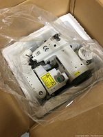 Top-down view of the white desk blindstitch machine inside cardboard box, protected by plastic bag and foam