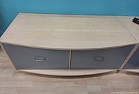 Front view of the cabinet showing its curved front grey drawer faces with metal handles and wood laminate top.