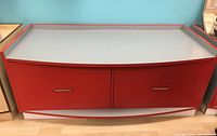 Red laminated cabinet with curved front and 2 large drawers closed, showing gray top with red edging and metal drawer handles.