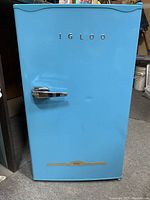 Front view of light blue Igloo retro refrigerator showing slight dents on the door and chrome handle.