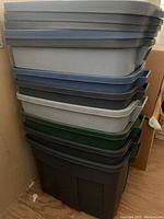 Stack of eight Rubbermaid Roughneck storage totes in various colors including gray, blue, green, and black.