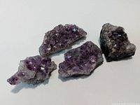 Photo showing 4 separate amethyst crystal clusters on a flat surface, highlighting their sizes, shapes, and purple crystal formations.