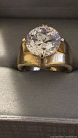 Front view of gold plated ring with large clear round stone on wide band