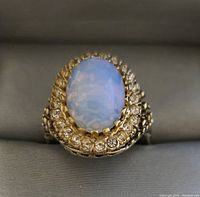 Close up image of the gold plated ring with opalite stone and rhinestone border on a neutral surface