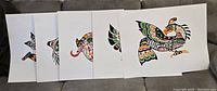 Five Indigenous art prints by John Nelson arranged side by side on a couch, showcasing vibrant colors and traditional Northwest Coast motifs.