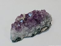 Photo showing a 5-inch amethyst crystal cluster with several well-formed purple crystals on a white and gray base.
