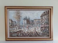 Full view of the framed oil painting showing a city street scene with buildings, trees, and people.