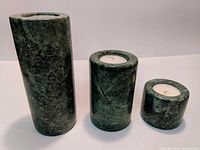 Image shows three cylindrical solid rock candle stick holders of different heights with tealight candles, texture green and dark gray in color.