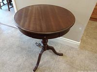 Front view of the round wooden table showing top surface and three supporting legs.