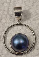 Front view of sterling silver pendant with blue pearl set in circular frame on grey textured background
