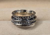 Close-up photo of the sterling silver spinner ring showing the three distinct bands; the middle band with beaded texture can spin independently from the engraved swirl patterned bands above and below.