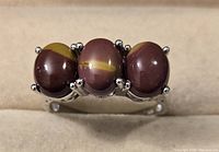 Close view of the sterling silver ring with three oval polished stones showing maroon and yellow banding, set with prongs in a decorative silver band.