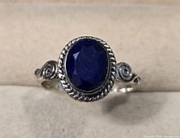 Close-up of sterling silver ring with oval dark blue faceted stone and rope bezel setting on a fabric background.
