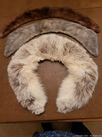 Three vintage fur collars laid out flat on a brown surface, showing cream, grey, and brown fur variations.