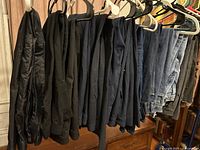 Photo of hanging women’s pants showing black, navy, dark blue, denim jeans, and brown pants visible on hangers.