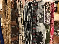 Eight scarves hanging on a rack showing different colors, patterns, and fabrics including knits, plaids, and florals.