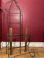 Full view of the wrought iron rack beside the stand against a reddish wall to show scale and detail of design.