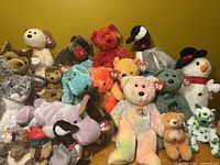 Pile of assorted Ty Beanie Babies and Beanie Buddies plush toys arranged against a yellow background, includes bears, dogs, penguins, rabbits, hippos, and more, each with original heart tag visible