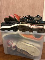 Shoes stacked on top of plastic bin showing various styles and colours.