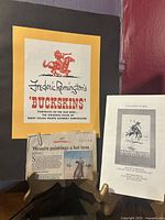 Folio cover labeled 'Frederic Remington's Buckskins' with a newspaper clipping about Western paintings and a gallery guide booklet.