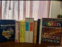 Bookshelf displaying cookbooks including Good Drinks (alcohol free), How to Cook Everything, The New Basic Cookbook, and The Grand Central Oyster Bar & Restaurant Seafood Cookbook.
