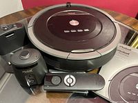 Photo showing iRobot Roomba 800 main vacuum unit, remote control, charging dock (missing cord), dustbin, and manual on table