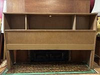 Front view of mid-century wooden headboard with shelving and compartments attached, seen in natural wood finish and placed on patterned floor.