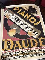 Photo showing the vintage Pianos Daude advertisement poster featuring a stylized pianist playing a keyboard from a top-down view.