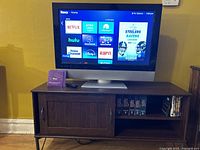 Polaroid TV on a wooden stand showing the Roku streaming interface on screen.