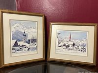 Two framed Austrian landscape prints depicting snowy mountain villages with churches, signed and numbered.
