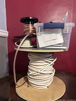 Large spool of white speaker cable, three smaller spools of speaker wire and plastic shoebox on a wooden surface