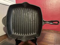 Full top-down view of square cast iron grill pan showing raised grilling ridges, single long handle, and small helper handle.