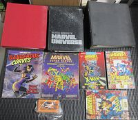 Overview photo of three binders (red, black, gray) and four Marvel Super Hero booklets plus a small card deck for role playing game materials.