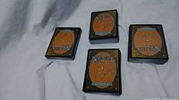 Four stacks of Magic: The Gathering cards showing the card back design, arranged on a light-colored cloth surface.