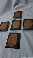 Five stacks of Magic The Gathering cards laid on a white fabric surface; card backs with logo and mana symbols visible.