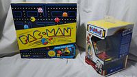 Pac-Man board game box on left, Dig Dug miniature tabletop video game box on right, showing front sides of both items.